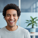 A happy person in their late 20s to early 30s smiling warmly at the camera. The background is softly blurred with blue and wh